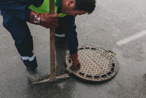 Slika prikazuje delavca, ki odpira kanalizacijski jašek.