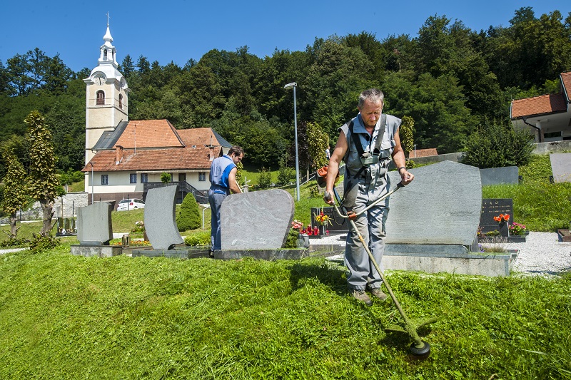 Moški kosi travo na pokopališču.