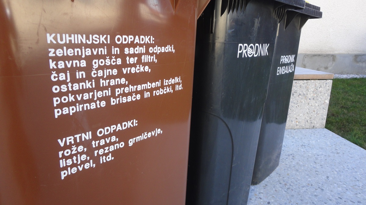 Na sliki je zabojnik za biološko razgradljive odpadke od blizu, v ozadju pa sta zabojnika za mešane odpadke in embalažo. 